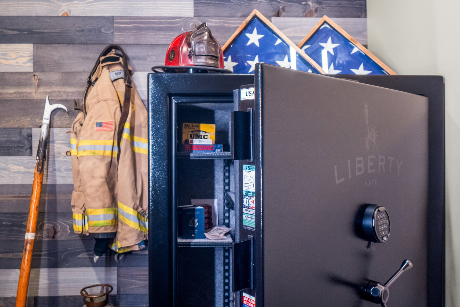 Open Liberty gun safe with electronic keypad lock storing ammunition, passports, and cash beside firefighter gear and folded American flags